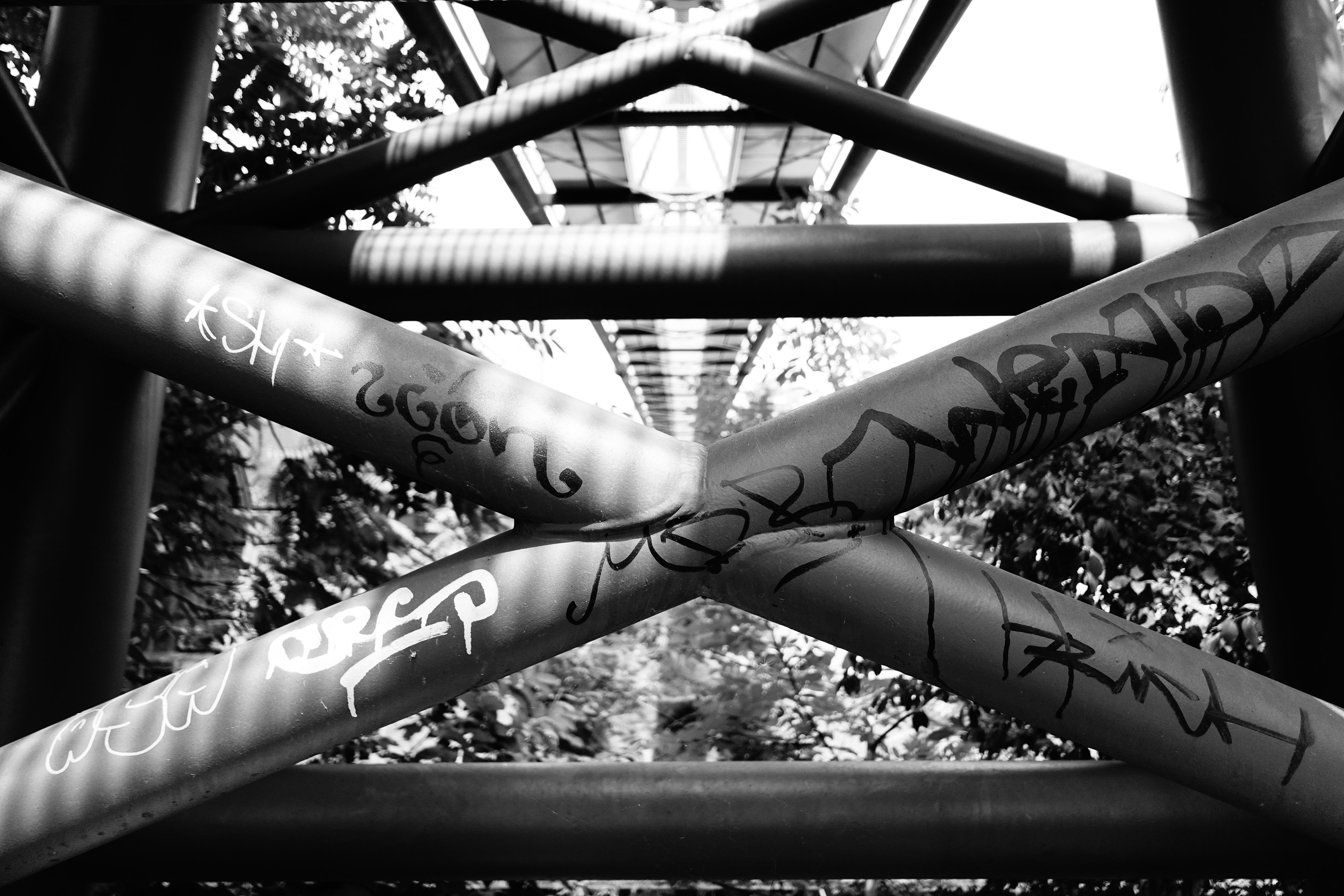 Black and white close-up of graffiti-covered steel bridge beams, creating an abstract geometric pattern.